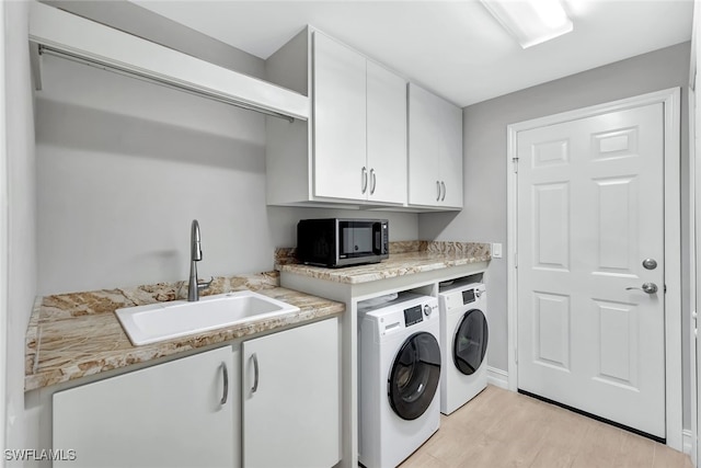 clothes washing area with washer and clothes dryer, cabinets, light wood-type flooring, and sink