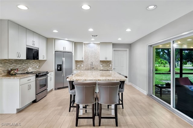 kitchen featuring a center island, white cabinets, light stone countertops, appliances with stainless steel finishes, and tasteful backsplash