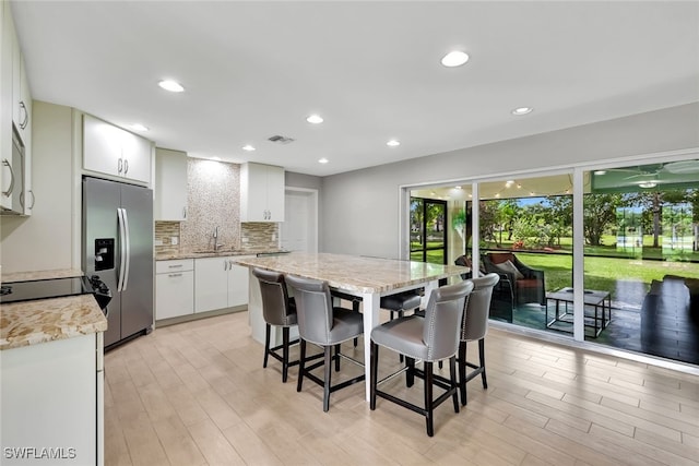 kitchen featuring stainless steel fridge, light wood-type flooring, backsplash, sink, and white cabinetry