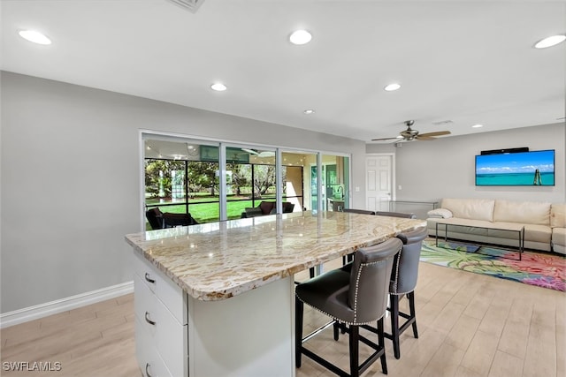 kitchen with a kitchen breakfast bar, light stone counters, a kitchen island, ceiling fan, and white cabinetry