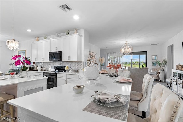 kitchen featuring stainless steel range with electric stovetop, a notable chandelier, pendant lighting, and a breakfast bar area