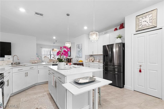 kitchen featuring stainless steel refrigerator with ice dispenser, sink, white cabinets, a kitchen island, and hanging light fixtures