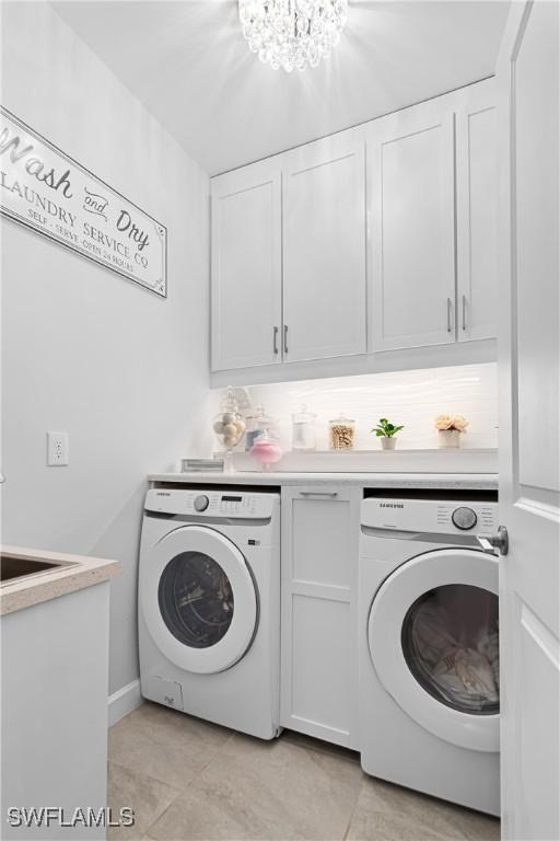 laundry room featuring washer and dryer, light tile patterned flooring, cabinets, and an inviting chandelier