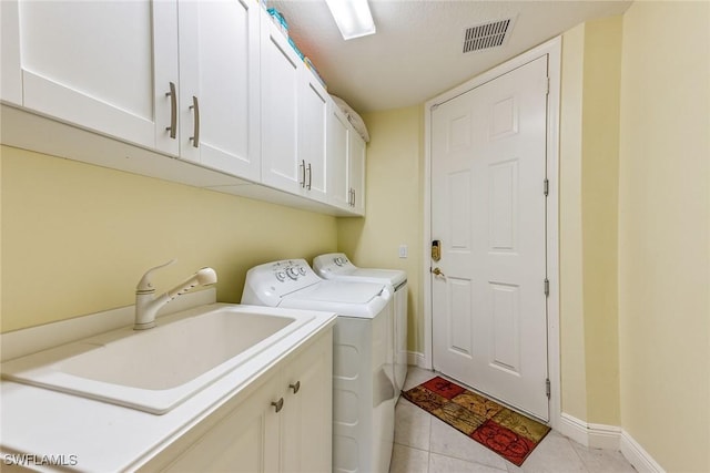 clothes washing area featuring sink, cabinets, washing machine and dryer, and light tile patterned floors