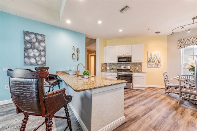 kitchen with stainless steel appliances, light wood-type flooring, kitchen peninsula, sink, and white cabinetry