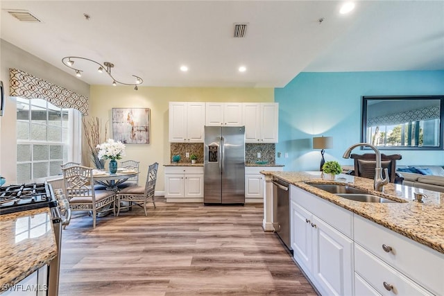 kitchen with sink, white cabinets, light hardwood / wood-style floors, light stone countertops, and appliances with stainless steel finishes