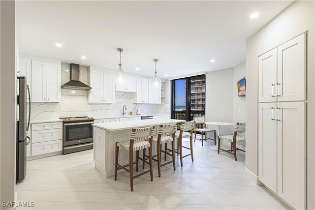 kitchen featuring white cabinets, stainless steel appliances, a kitchen island, and wall chimney exhaust hood