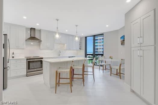 kitchen with light countertops, appliances with stainless steel finishes, floor to ceiling windows, wall chimney exhaust hood, and pendant lighting