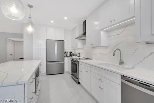 kitchen featuring light stone counters, white cabinetry, hanging light fixtures, appliances with stainless steel finishes, and wall chimney exhaust hood