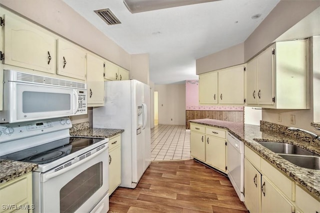 kitchen with sink, white appliances, cream cabinetry, dark stone counters, and light wood-type flooring