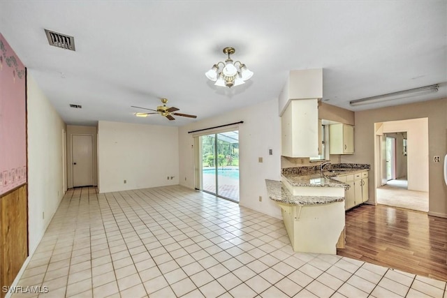 kitchen with ceiling fan with notable chandelier, sink, dark stone counters, light tile patterned floors, and kitchen peninsula