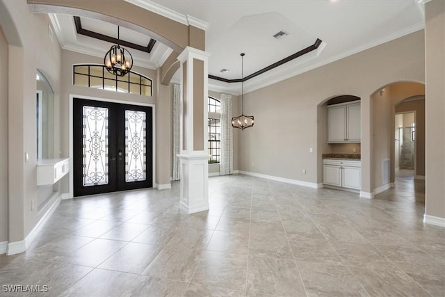 entryway with a raised ceiling, crown molding, a chandelier, and french doors