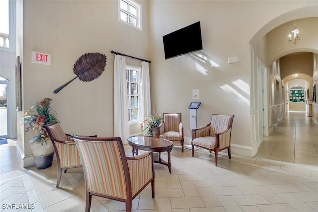 sitting room with baseboards, arched walkways, a towering ceiling, and light tile patterned floors