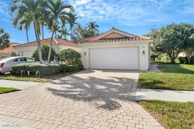 mediterranean / spanish-style house featuring a garage, stucco siding, a tile roof, and decorative driveway