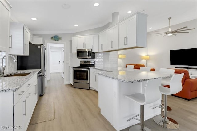 kitchen featuring a peninsula, open floor plan, a sink, light wood-style flooring, and stainless steel appliances
