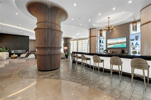 interior space featuring hanging light fixtures, an inviting chandelier, a raised ceiling, tile patterned floors, and a breakfast bar