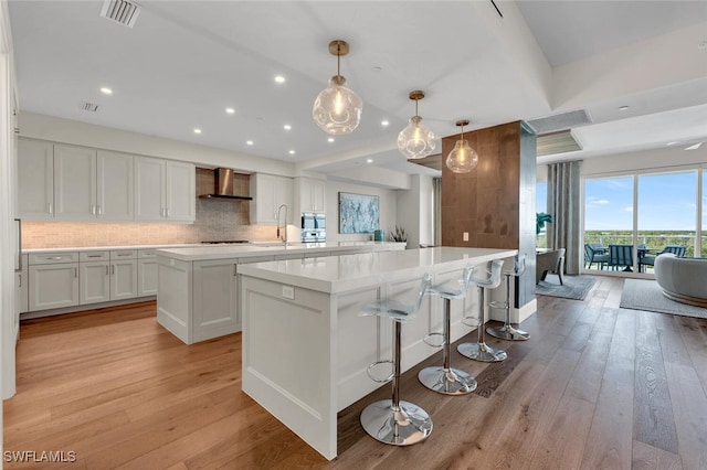 kitchen featuring white cabinetry, wall chimney range hood, backsplash, a spacious island, and decorative light fixtures