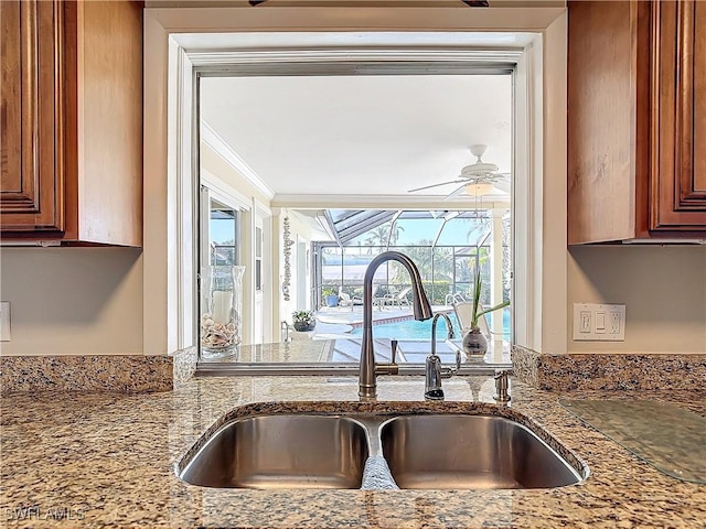 kitchen featuring light stone countertops, ceiling fan, crown molding, and sink