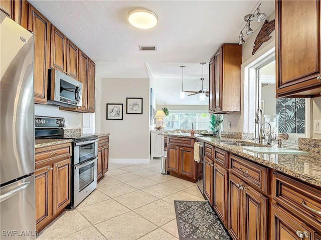 kitchen featuring appliances with stainless steel finishes, light stone counters, ceiling fan, sink, and light tile patterned floors