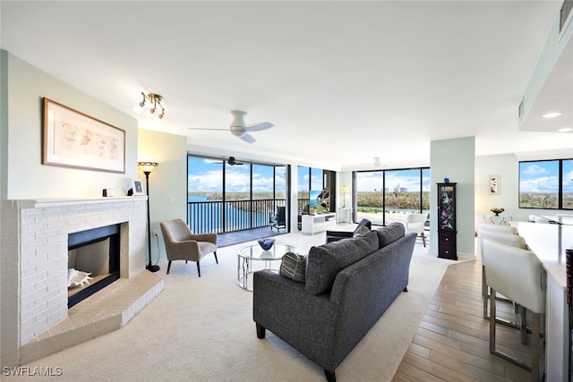 living room featuring a brick fireplace, a wall of windows, and ceiling fan