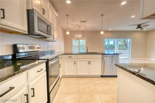 kitchen with dark stone counters, ceiling fan with notable chandelier, sink, appliances with stainless steel finishes, and decorative light fixtures