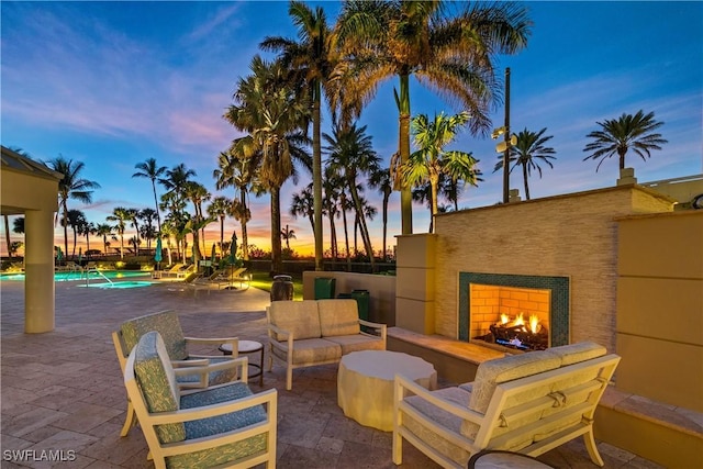 patio terrace at dusk featuring an outdoor living space with a fireplace and a community pool