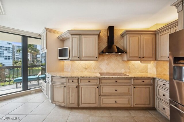 kitchen featuring black electric stovetop, wall chimney range hood, light stone countertops, light tile patterned floors, and stainless steel fridge with ice dispenser