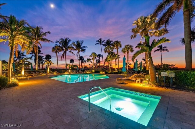 pool at dusk with a community hot tub and a patio