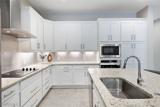 kitchen with white cabinets, appliances with stainless steel finishes, backsplash, and wall chimney range hood