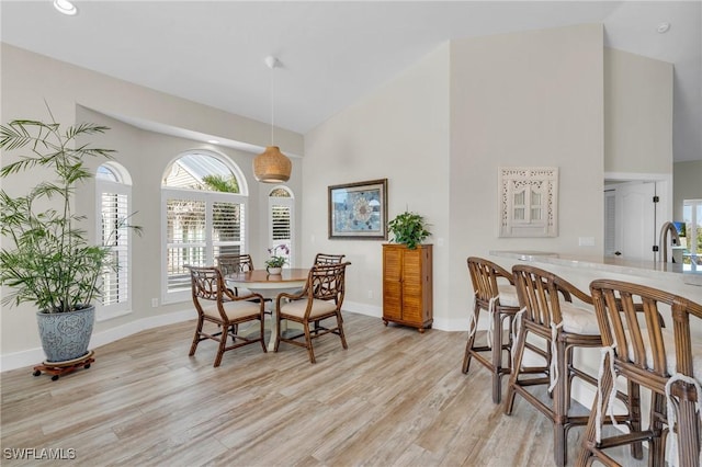 dining room featuring light wood-type flooring, sink, and high vaulted ceiling