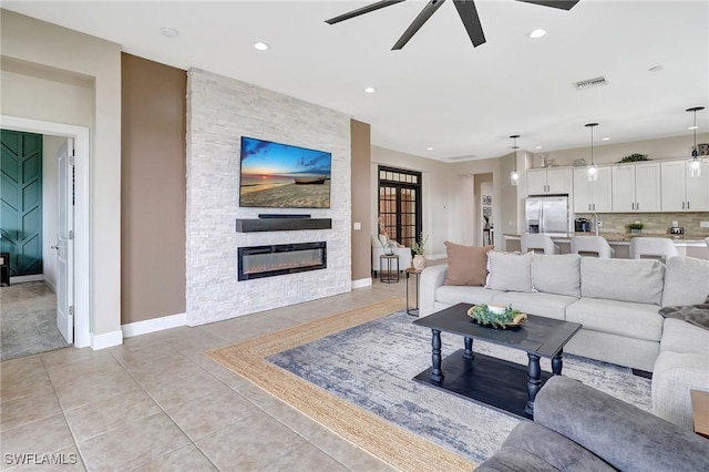 tiled living room with ceiling fan and a stone fireplace