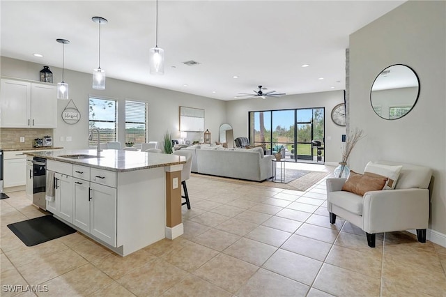 kitchen with pendant lighting, white cabinets, sink, ceiling fan, and light stone counters