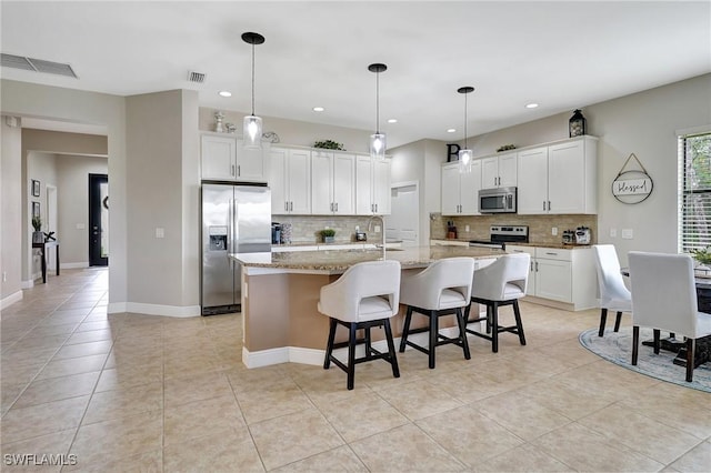 kitchen featuring white cabinets, a kitchen island with sink, appliances with stainless steel finishes, and light tile patterned floors