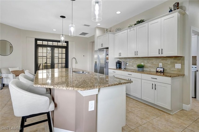 kitchen with decorative light fixtures, sink, a kitchen island with sink, stainless steel fridge with ice dispenser, and white cabinets