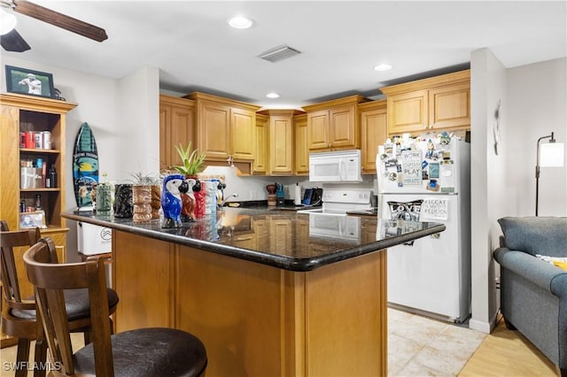 kitchen featuring kitchen peninsula, a kitchen bar, white appliances, ceiling fan, and dark stone countertops