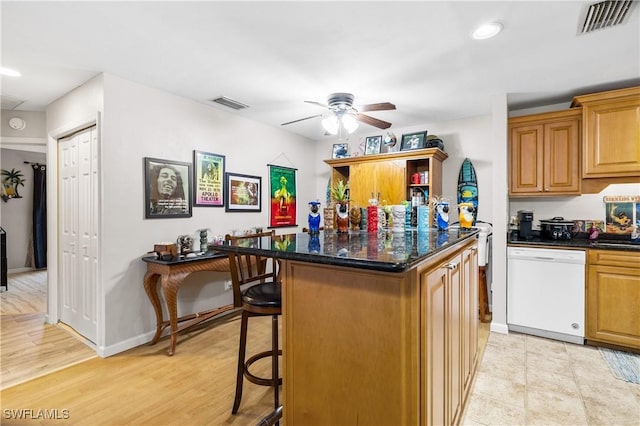 kitchen with ceiling fan, dishwasher, dark stone countertops, a breakfast bar, and a kitchen island