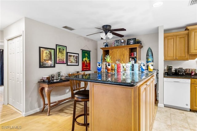 kitchen with ceiling fan, dark stone countertops, white dishwasher, a breakfast bar, and a kitchen island