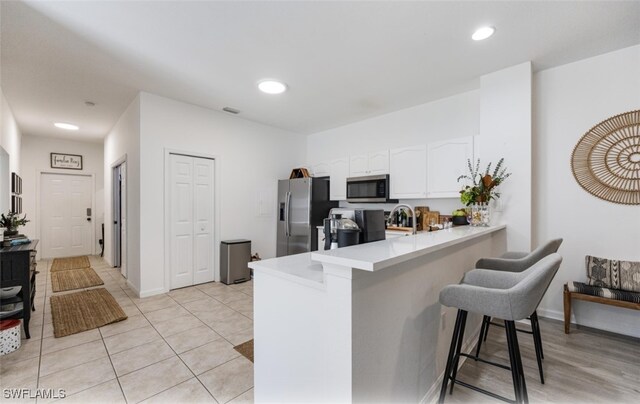 kitchen featuring kitchen peninsula, appliances with stainless steel finishes, a breakfast bar, light tile patterned floors, and white cabinets