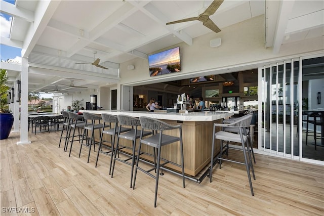 bar featuring ceiling fan, a dry bar, beam ceiling, and light wood-style floors