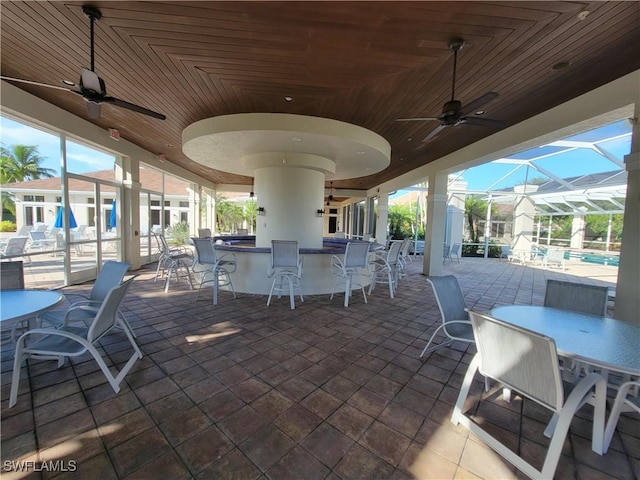 view of patio with ceiling fan, exterior bar, and glass enclosure