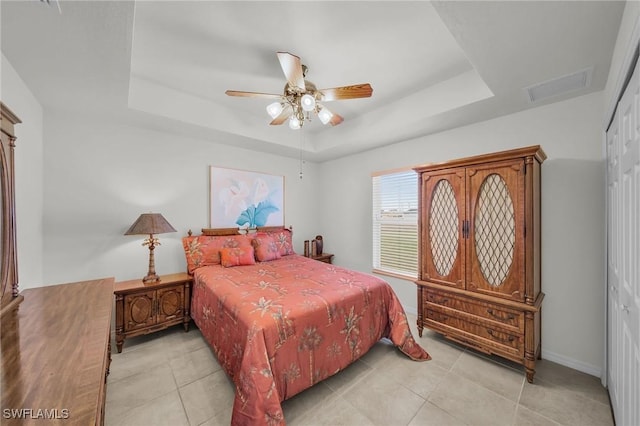 bedroom featuring ceiling fan, a closet, light tile patterned floors, and a tray ceiling