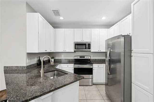 kitchen with appliances with stainless steel finishes, dark stone counters, sink, light tile patterned floors, and white cabinets