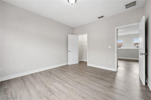 unfurnished bedroom featuring a spacious closet, wood-type flooring, and a closet