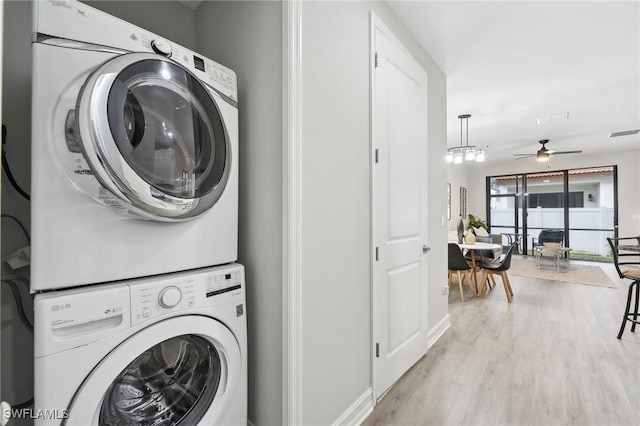 washroom featuring ceiling fan with notable chandelier, light hardwood / wood-style floors, and stacked washer / dryer