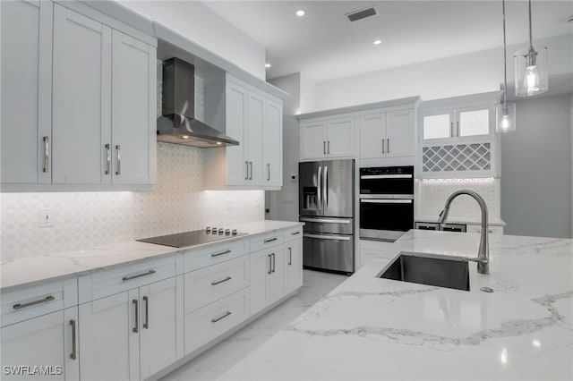 kitchen with sink, wall chimney range hood, pendant lighting, white cabinets, and appliances with stainless steel finishes