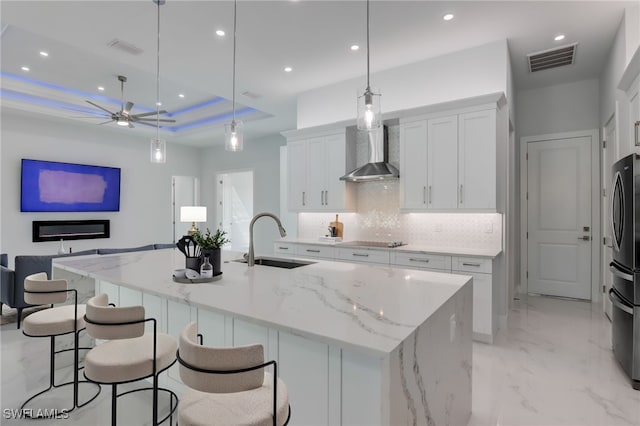 kitchen with white cabinetry, sink, decorative light fixtures, and wall chimney range hood