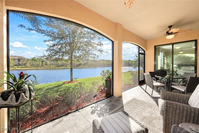 sunroom with ceiling fan and a water view