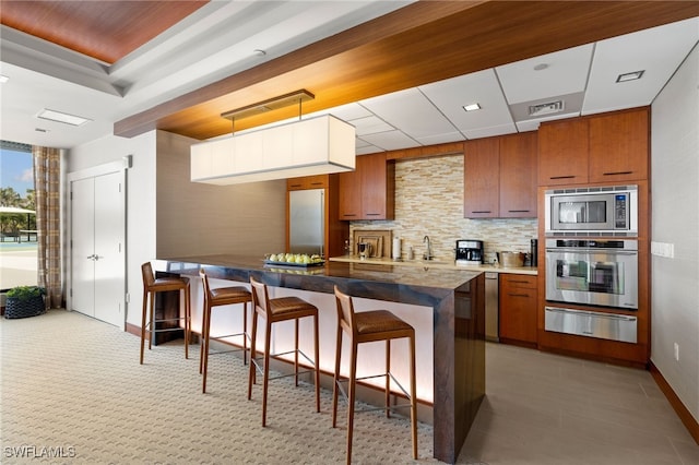 kitchen featuring hanging light fixtures, stainless steel appliances, a kitchen breakfast bar, kitchen peninsula, and decorative backsplash