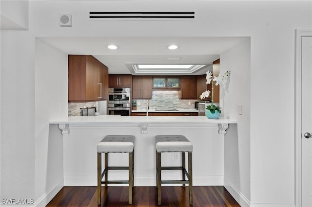 kitchen featuring a breakfast bar, decorative backsplash, double oven, dark hardwood / wood-style flooring, and kitchen peninsula