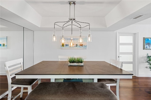 dining area with a raised ceiling and dark wood-type flooring